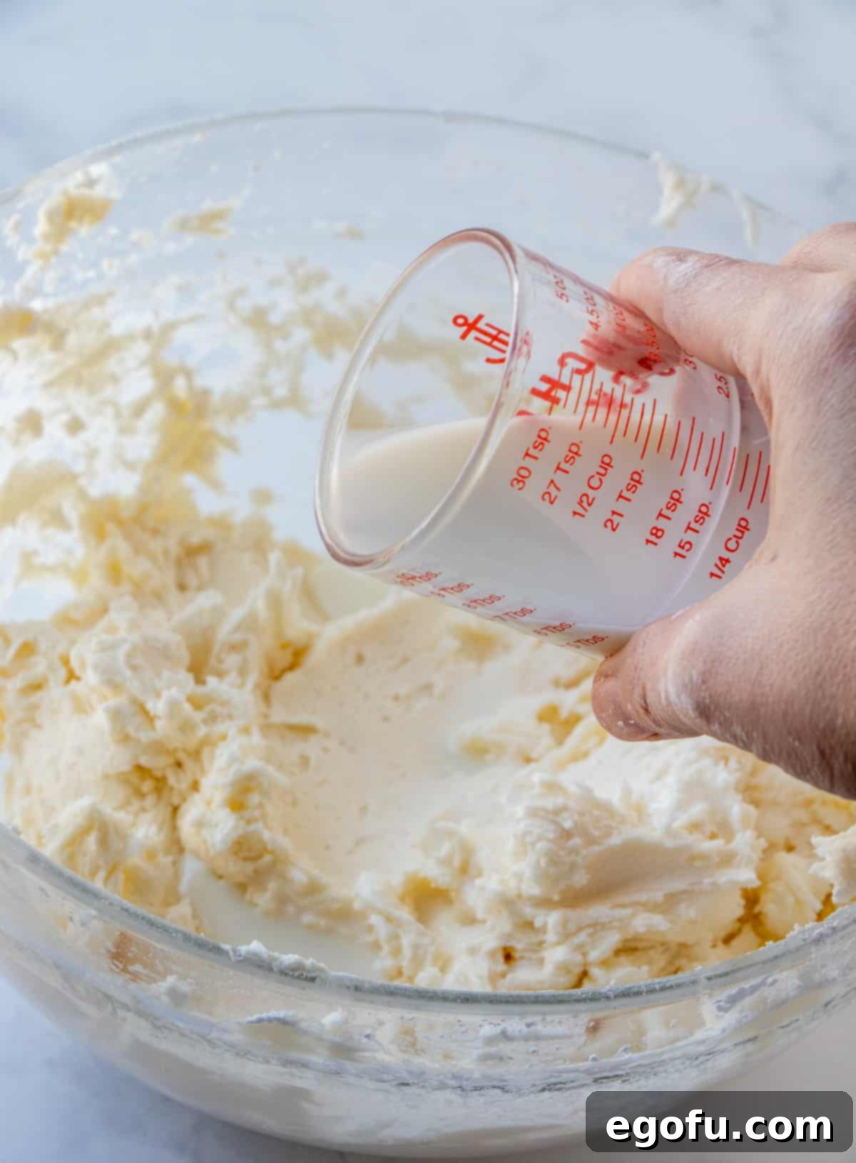 Velvet Banana Delight Cupcakes 16 Milk being gradually added to the buttercream frosting mixture to achieve the perfect consistency.