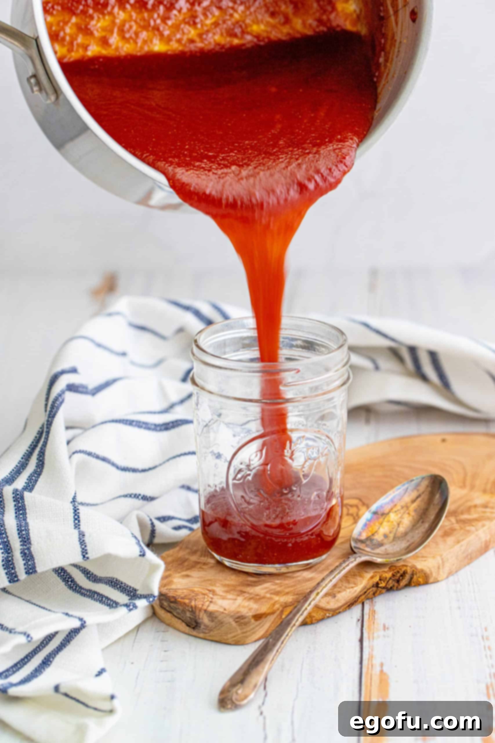 BBQ Sauce being poured into jar on wooden board with spoon