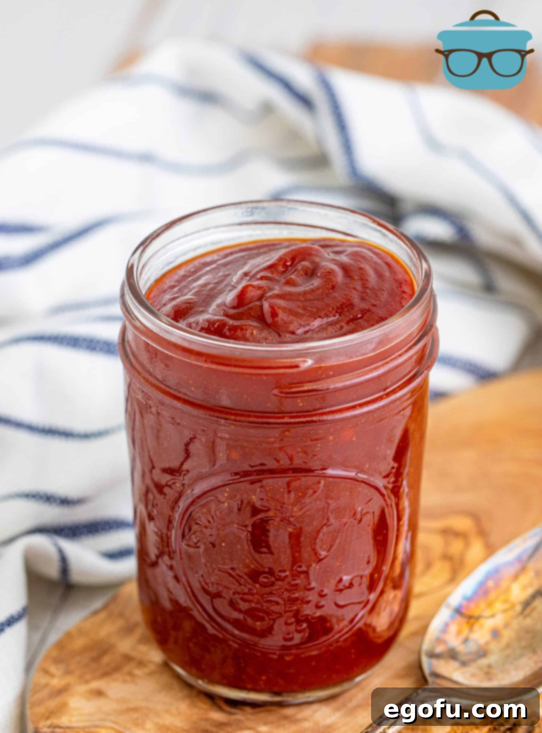 Homemade BBQ Sauce ini jar on wooden board with spoon next to it