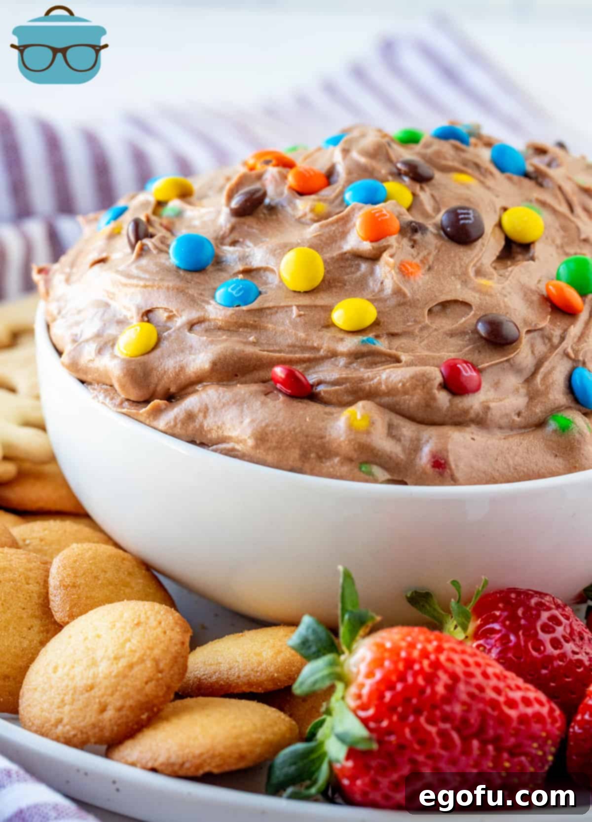 M&M Brownie Batter Dip in bowl surrounded by fruit and cookies, showcasing a delicious and easy dessert.