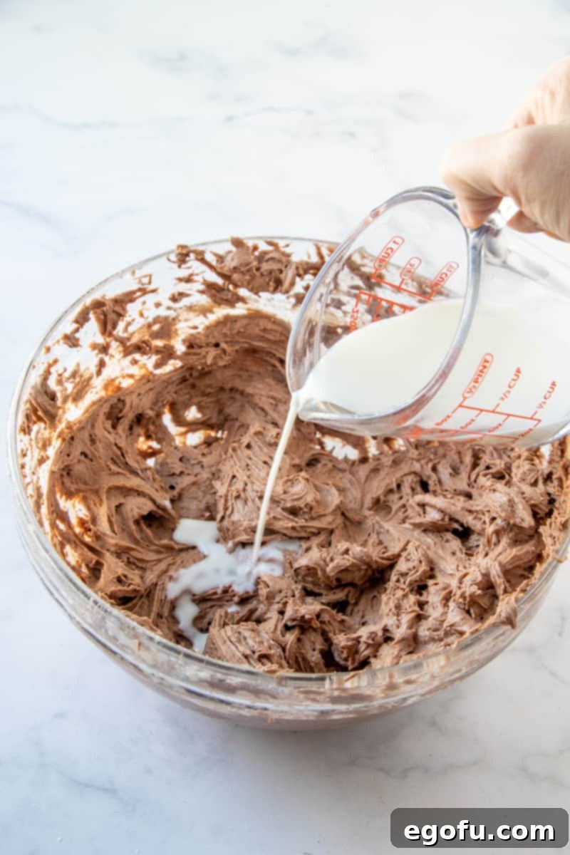A hand pouring milk into the brownie batter mixture to achieve the perfect consistency.