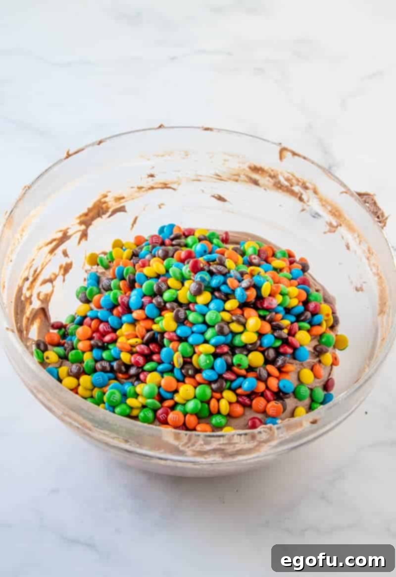 Mini M&M's added to the clear bowl with the finished brownie batter mixture, ready to be folded in.