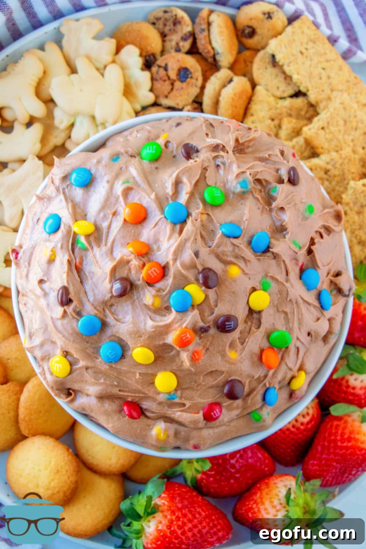 Overhead shot of M&M Brownie Batter Dip Recipe in a bowl surrounded by fruit, cookies, and crackers, creating an inviting spread.