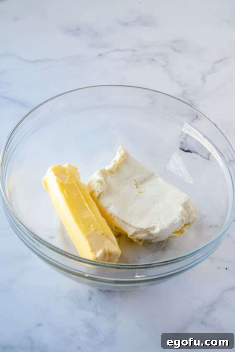 Softened butter and cream cheese ready for mixing in a clear bowl.