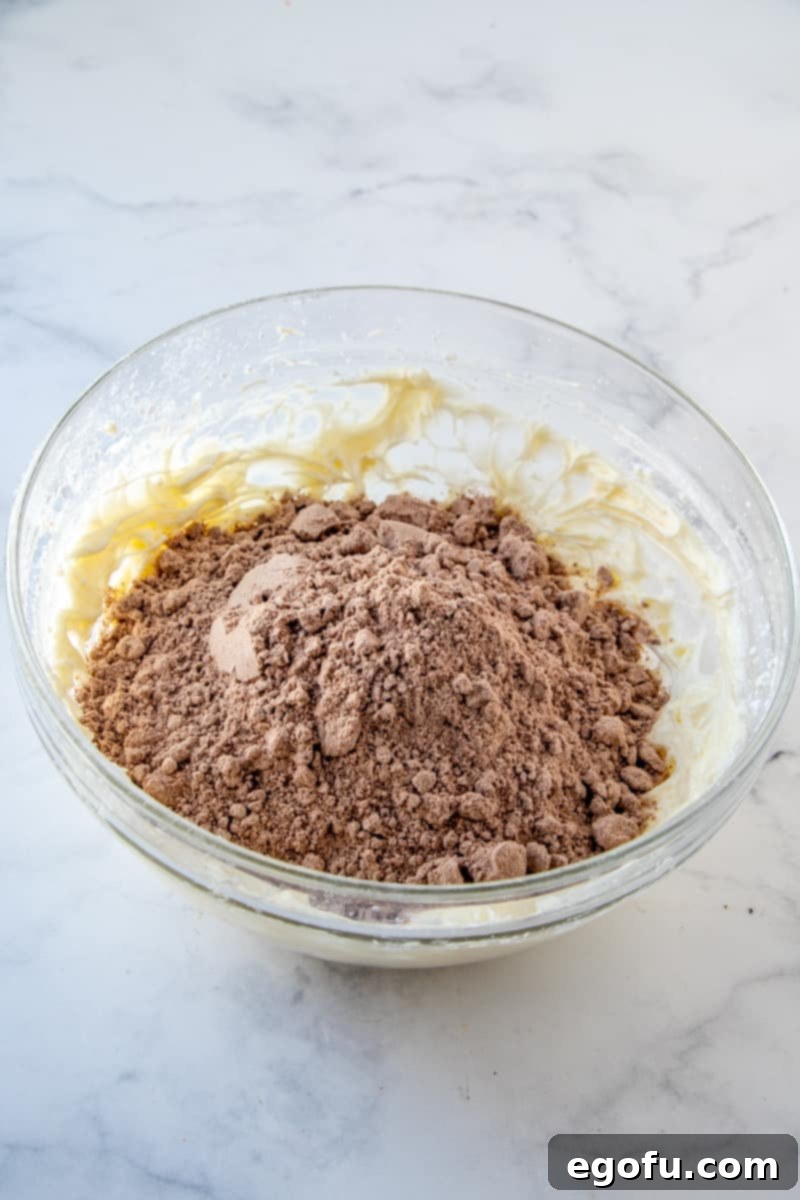 Dry brownie mix added to the creamy base in a clear bowl, ready to be beaten.
