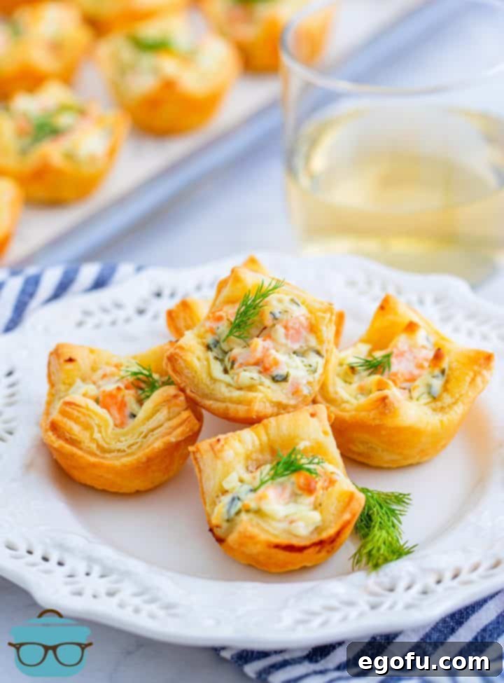 Four golden Smoked Salmon Puff Pastry Bites on a white plate, garnished with fresh dill.