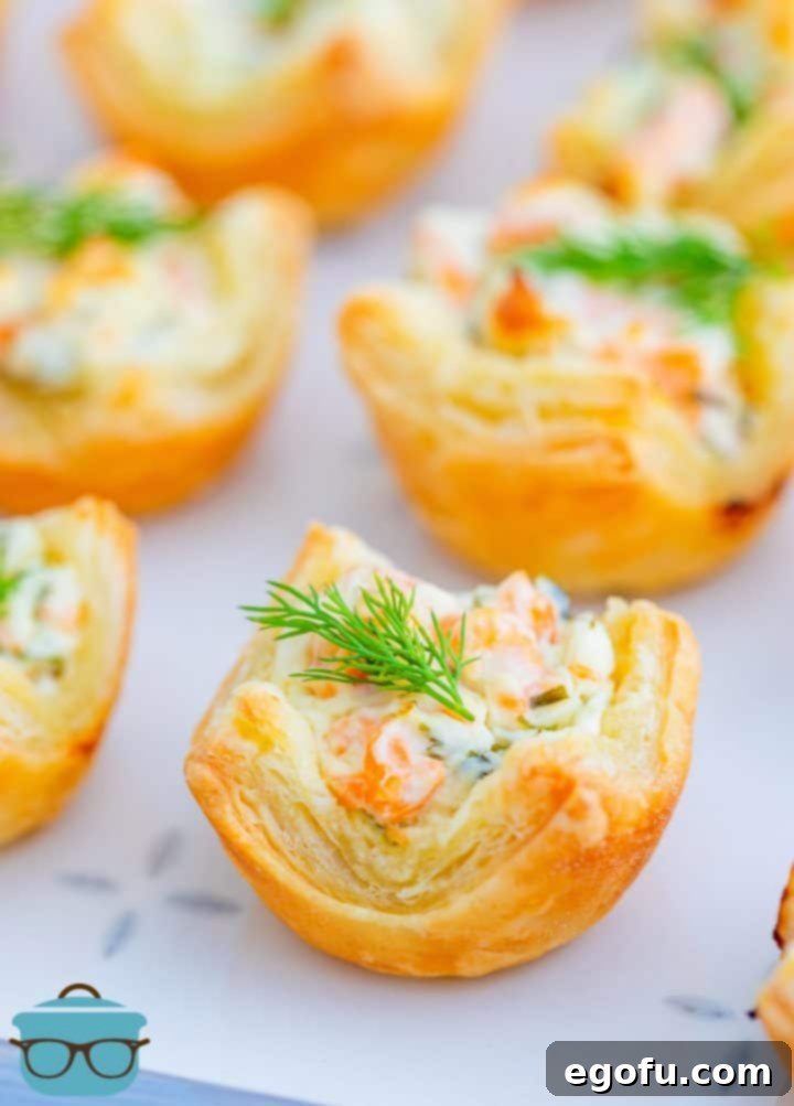 A close-up of Smoked Salmon Puff Pastry Bites topped with fresh dill on an elegant serving platter.
