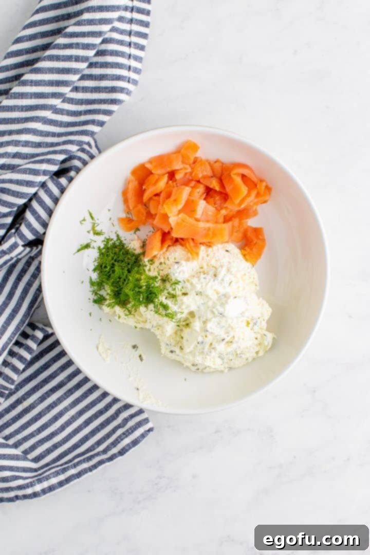 Smoked salmon, fresh dill, and whipped chive cream cheese combined in a white bowl, ready for mixing.