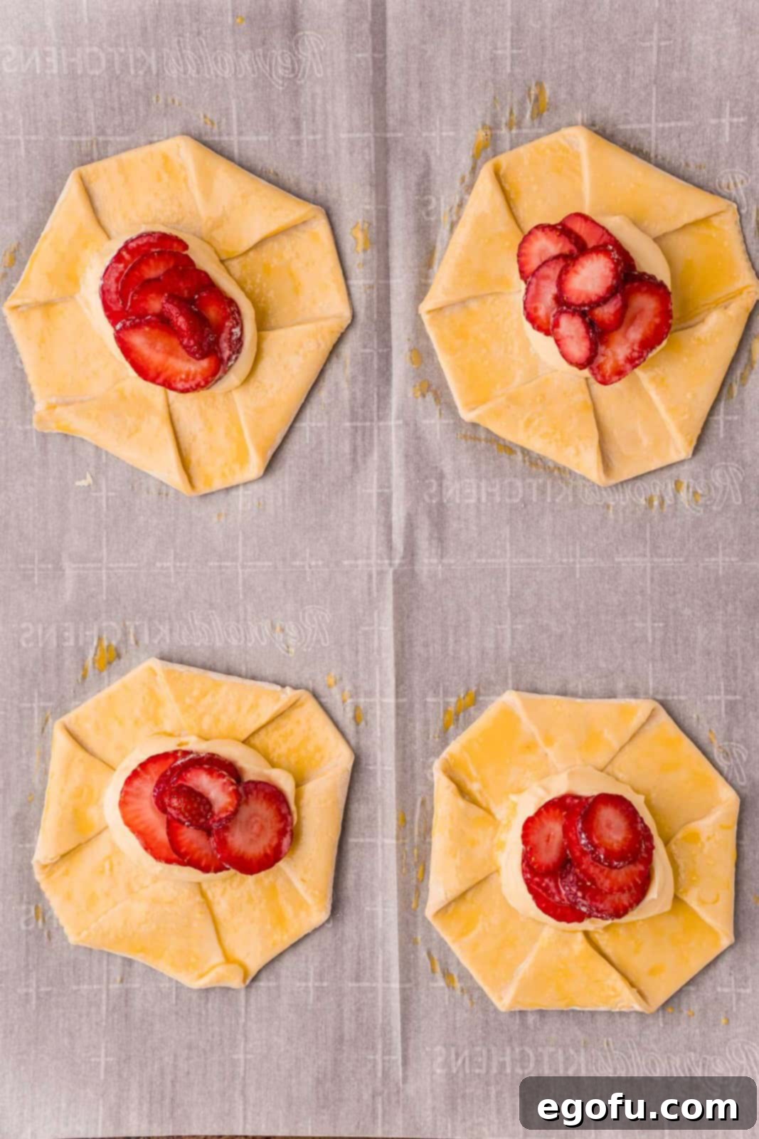 Unbaked danishes, now fully assembled with luscious strawberries and creamy cheese mixture, arranged on a parchment-lined baking sheet, ready for the oven.