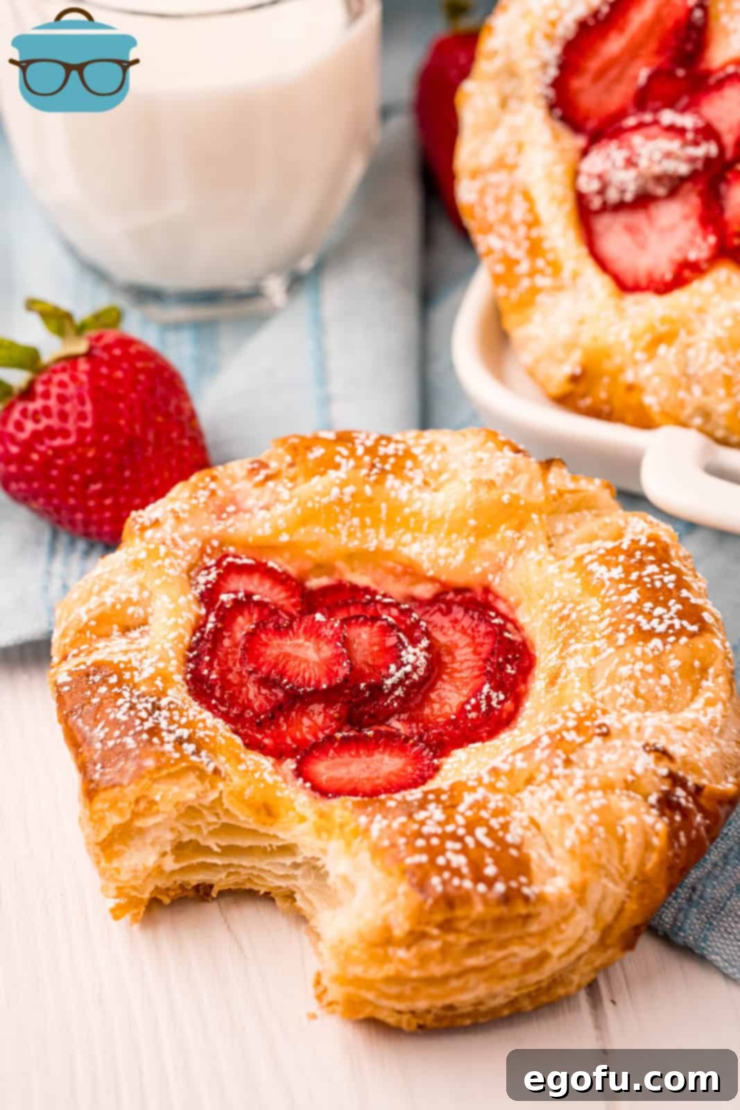 A delicious Strawberry Cheese Danish with a bite taken out, revealing the flaky pastry and vibrant filling, garnished with powdered sugar.