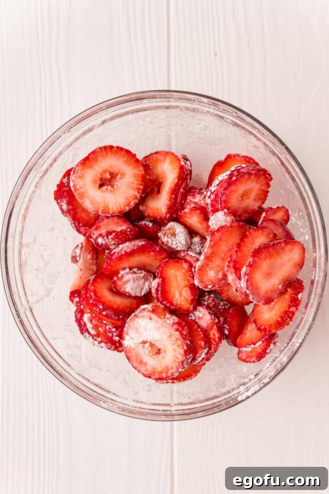 Sliced strawberries in a bowl, coated with a mixture of cornstarch and sugar, marinating to develop flavor.