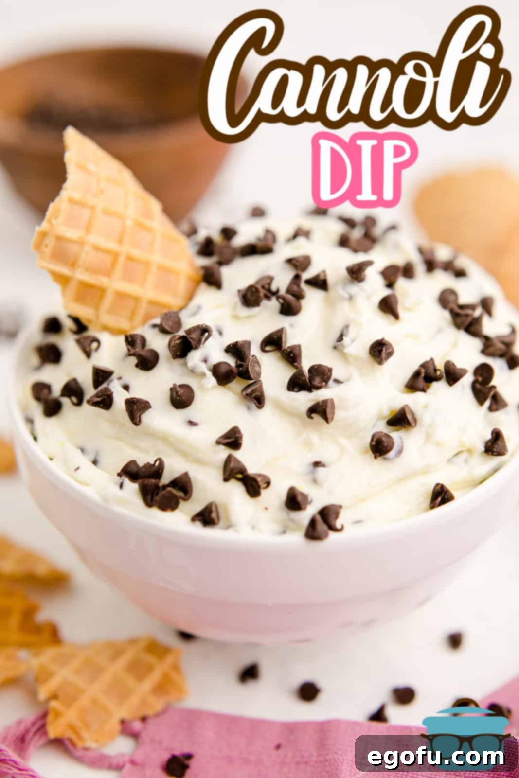 A finished Cannoli Dip in a pristine white bowl, adorned with chocolate chips and a broken waffle cone piece, perfect for sharing on Pinterest.