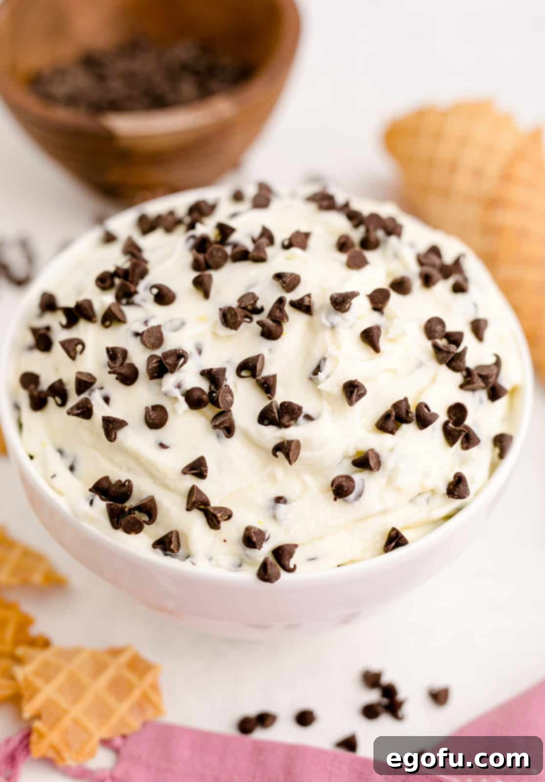 The inviting Cannoli Dip, glistening in a white bowl, elegantly surrounded by a scattering of crisp waffle cones, ready to be enjoyed.