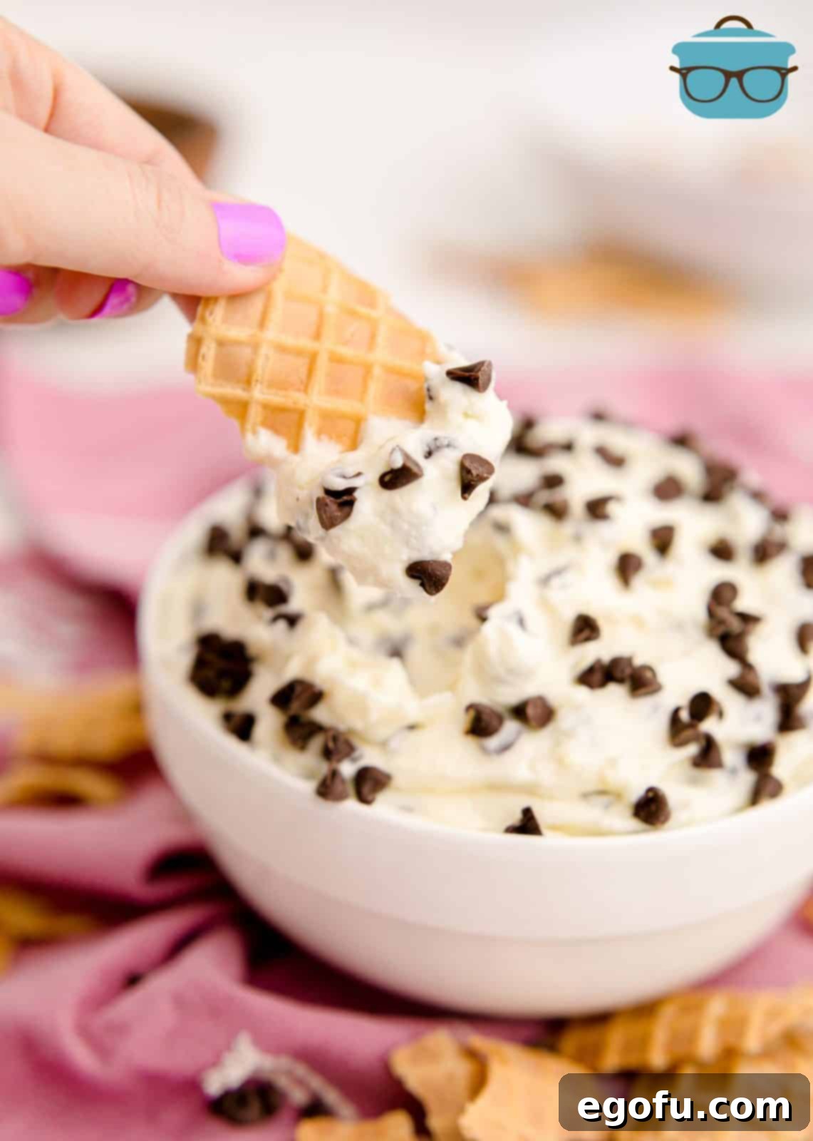 A hand gracefully dipping a broken piece of waffle cone into the luscious Cannoli Dip, inviting a taste.
