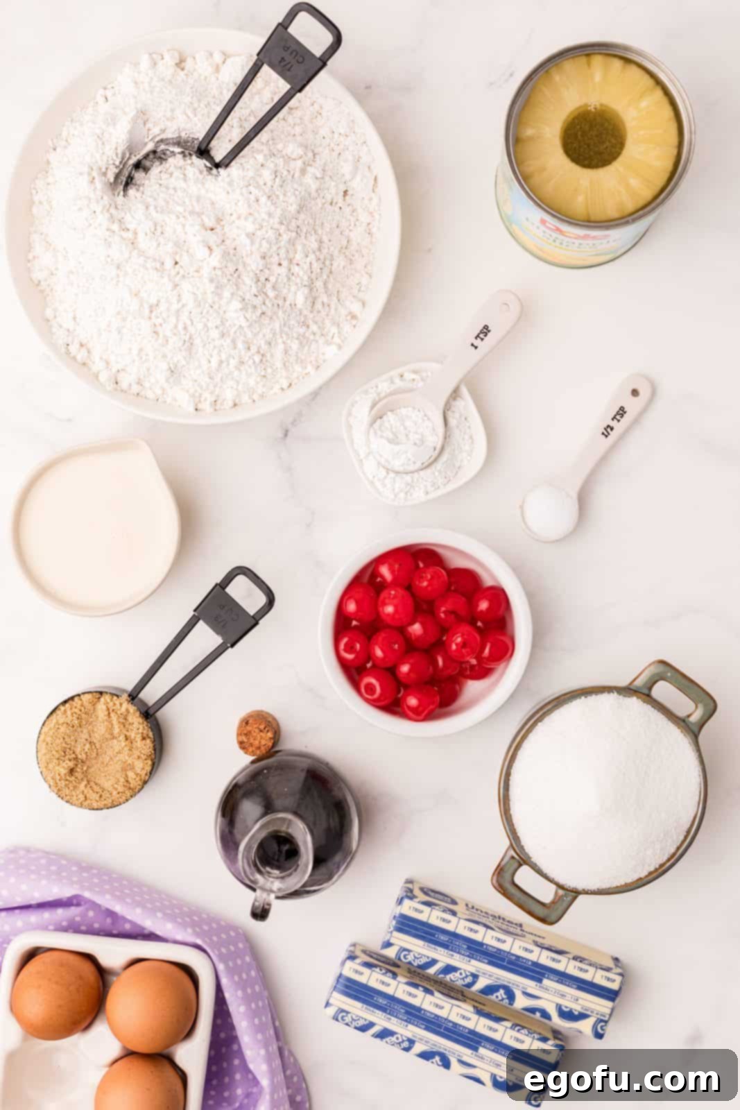 Sunshine Pineapple Bundt Cake 4 Arrangement of all fresh and packaged ingredients for Pineapple Upside Down Bundt Cake, including butter, brown sugar, pineapple rings, maraschino cherries, cake flour, baking powder, salt, granulated sugar, eggs, vanilla extract, evaporated milk, and pineapple juice.