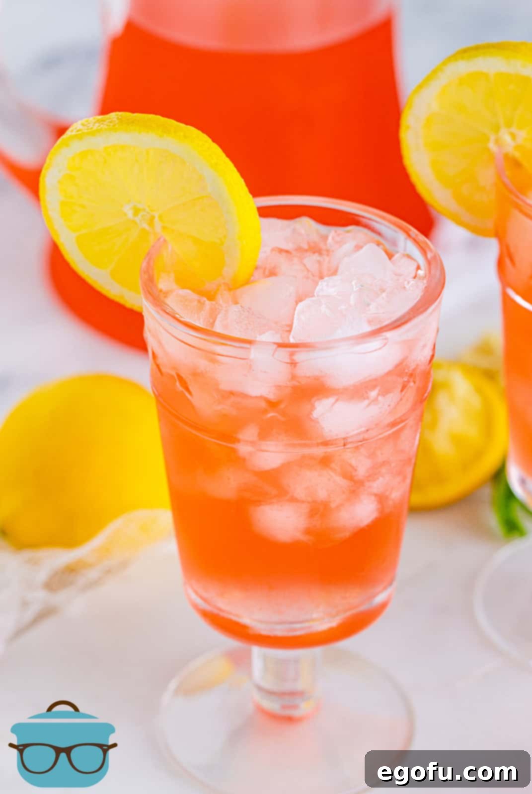 A glass of Pink Lemonade Recipe with ice and a lemon garnish, sitting on a table.