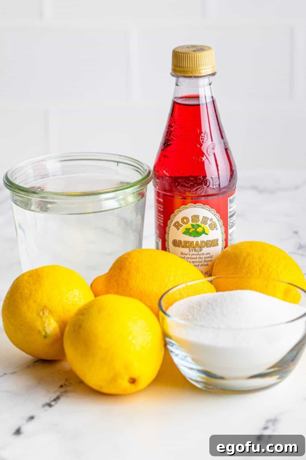 Ingredients needed to make Homemade Pink Lemonade laid out: water, granulated sugar, freshly squeezed lemon juice, and a bottle of grenadine.