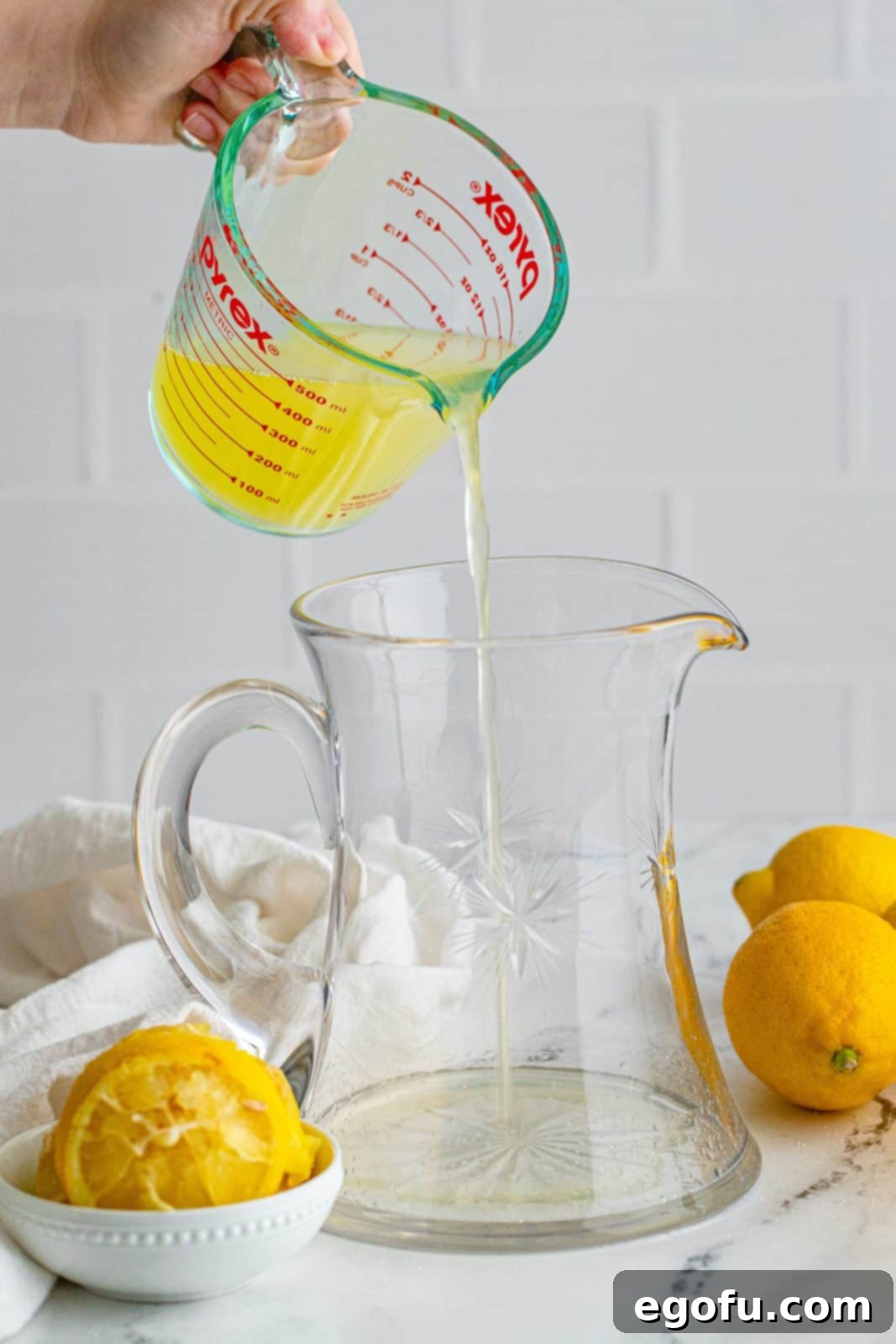 Freshly squeezed lemon juice being poured into a clear pitcher.