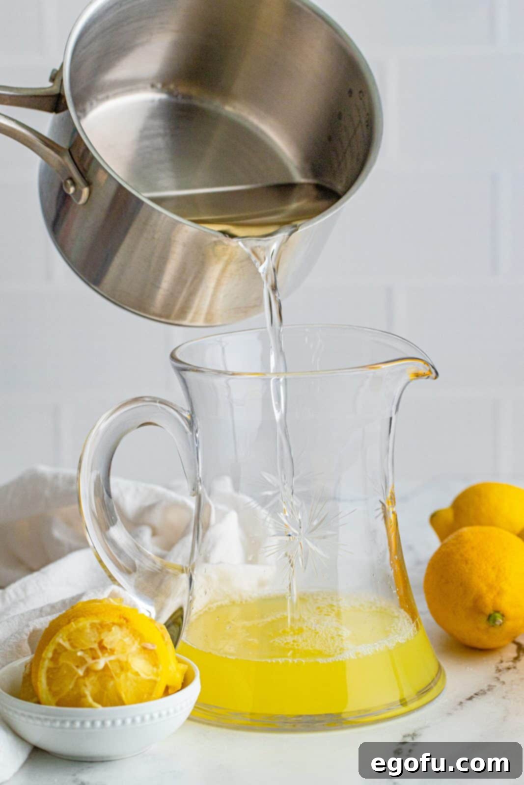 The simple syrup (sugar water) being poured into the pitcher containing lemon juice.