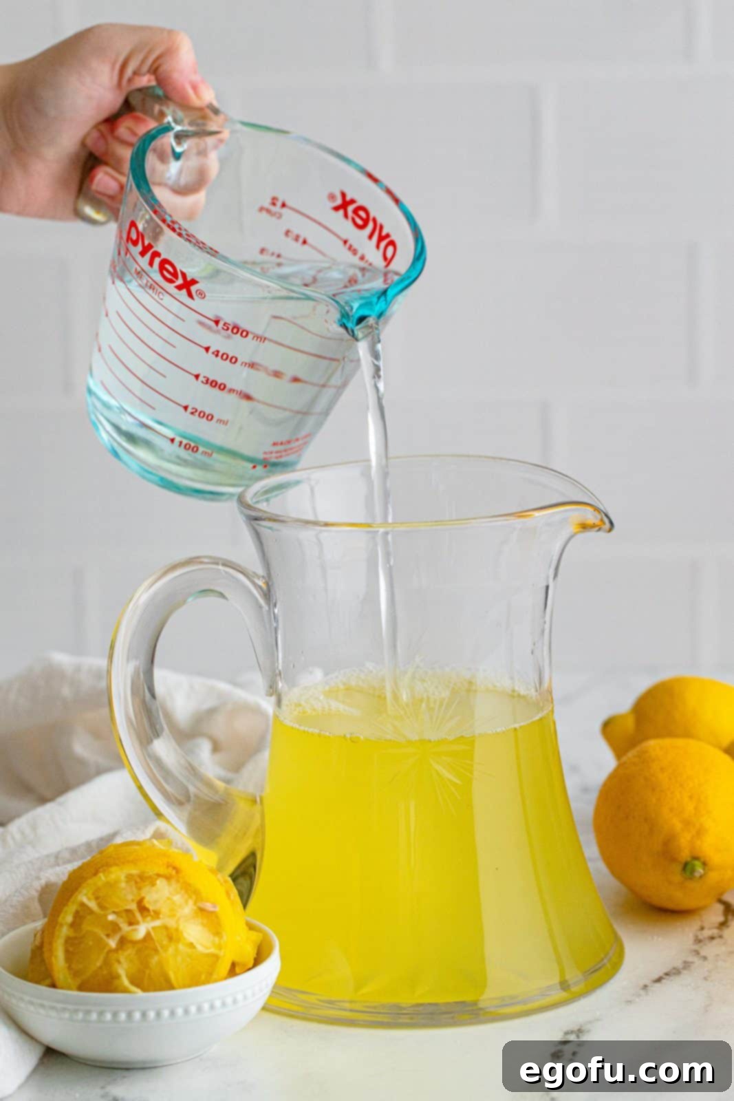 The remaining plain water being poured into the pitcher with the lemon and sugar mixture.