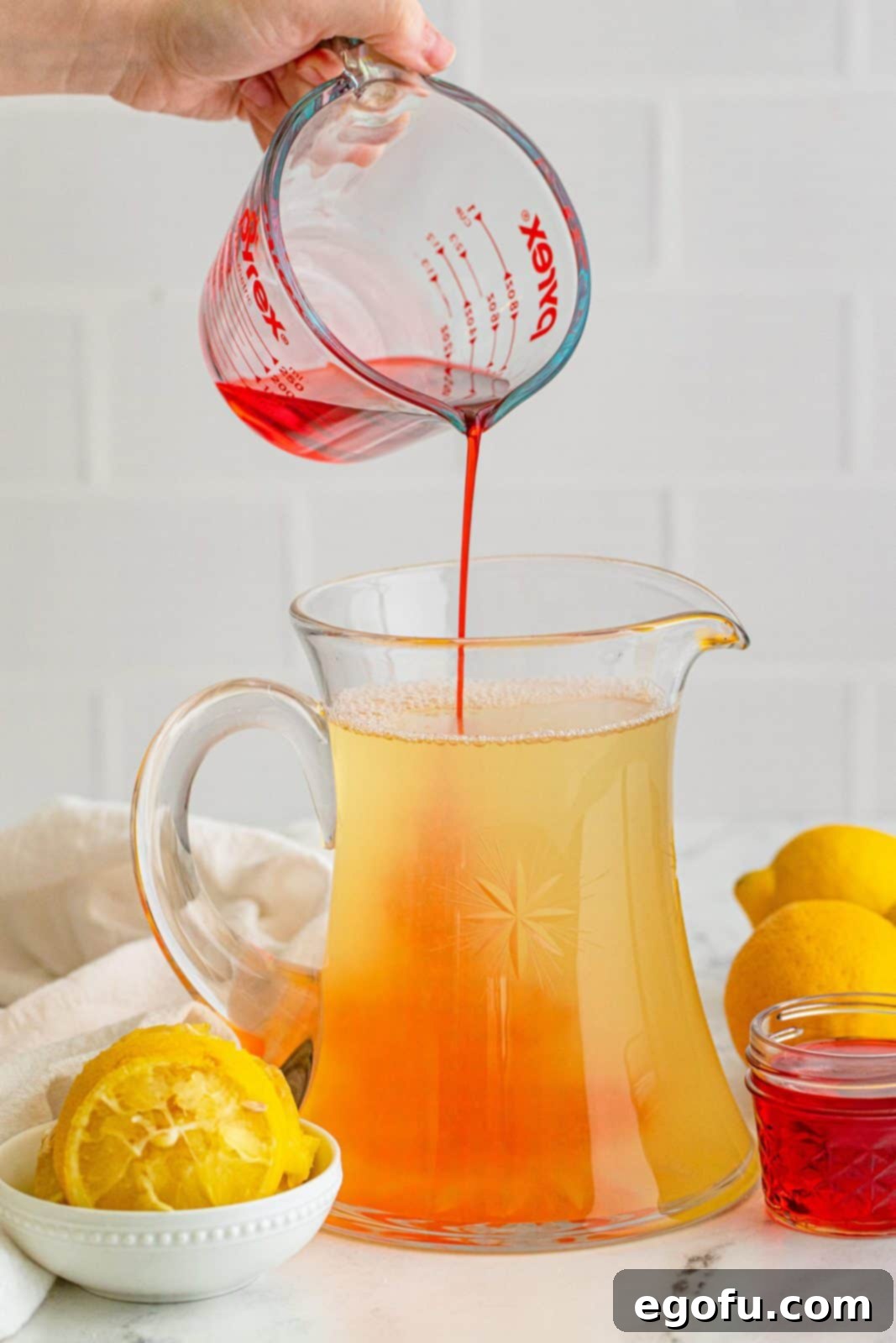 Grenadine being poured into the pitcher, tinting the lemonade pink.