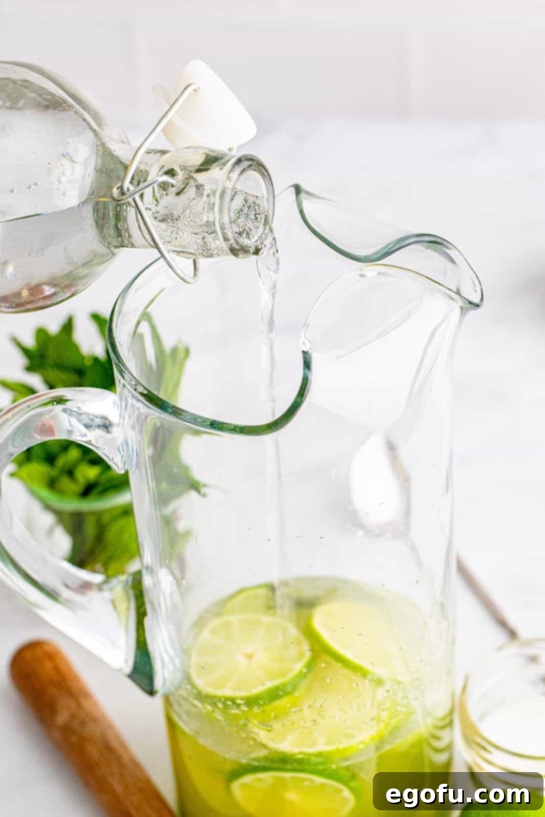 Clear club soda being poured into a pitcher, adding effervescence to the Mojito mixture.