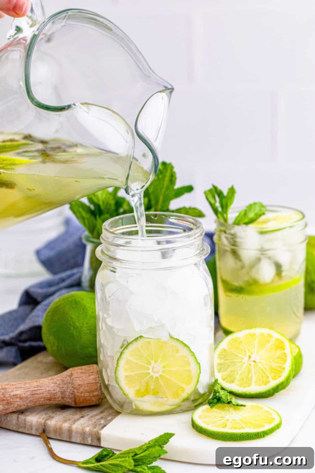 A pitcher pouring a vibrant Summer Mojito cocktail into a mason jar filled with ice, garnished with mint and lime.