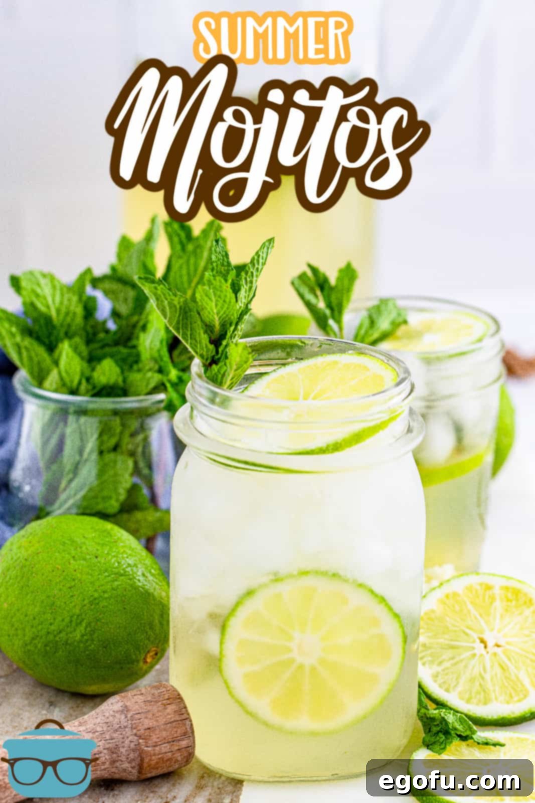 A close-up view of a glass filled with a refreshing Summer Mojito, adorned with lime wedges and fresh mint leaves, with a pitcher in the background.