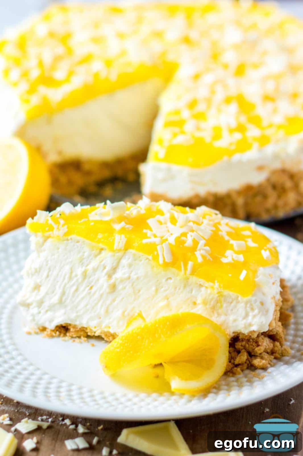Slice of No-Bake Lemon White Chocolate Cheesecake on white plate with slice of lemon.