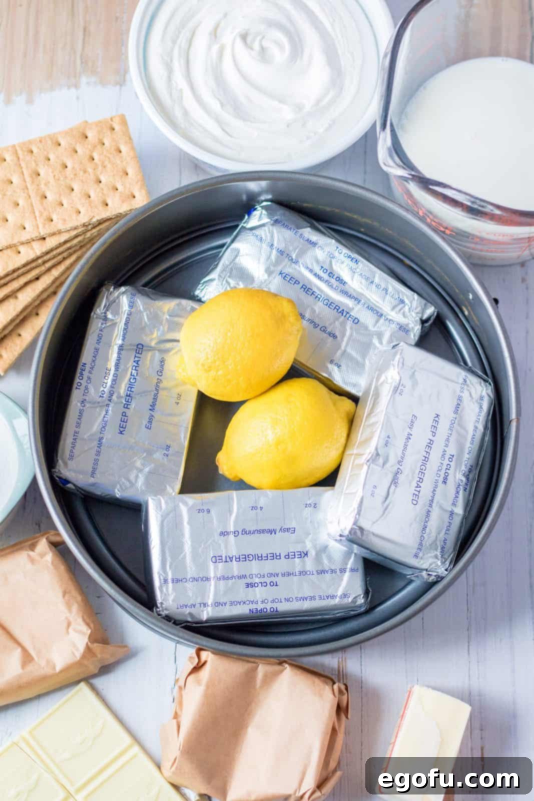 Ingredients needed: graham crackers, butter, white chocolate flavored instant pudding, milk, cream cheese, sugar, whipped topping, lemon, lemon instant pudding and a white chocolate bar.