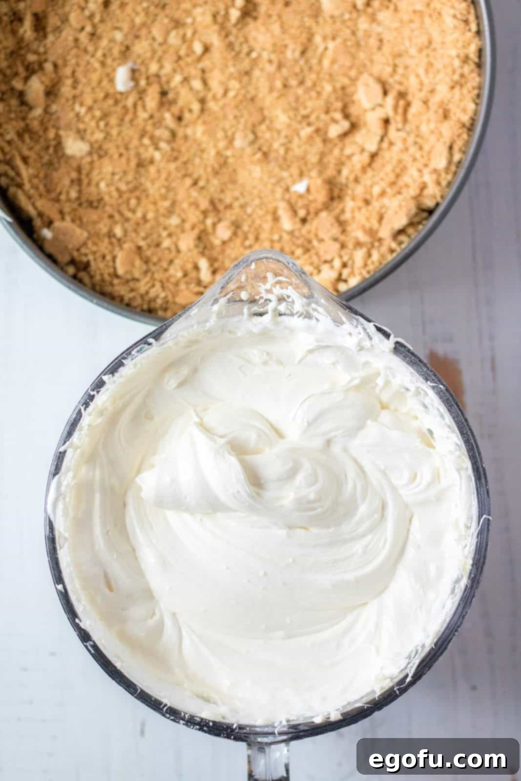 Mixed up cheesecake batter in bowl with crust in pan.