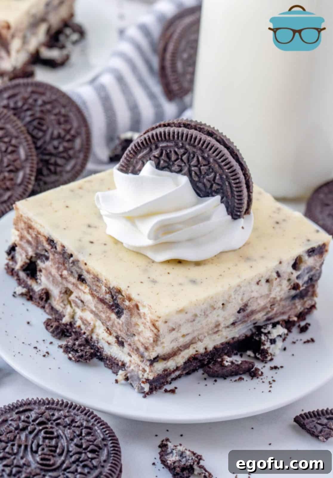 Slice of Oreo Cheesecake Bars on white plate topped with whipped topping and oreo cookie.