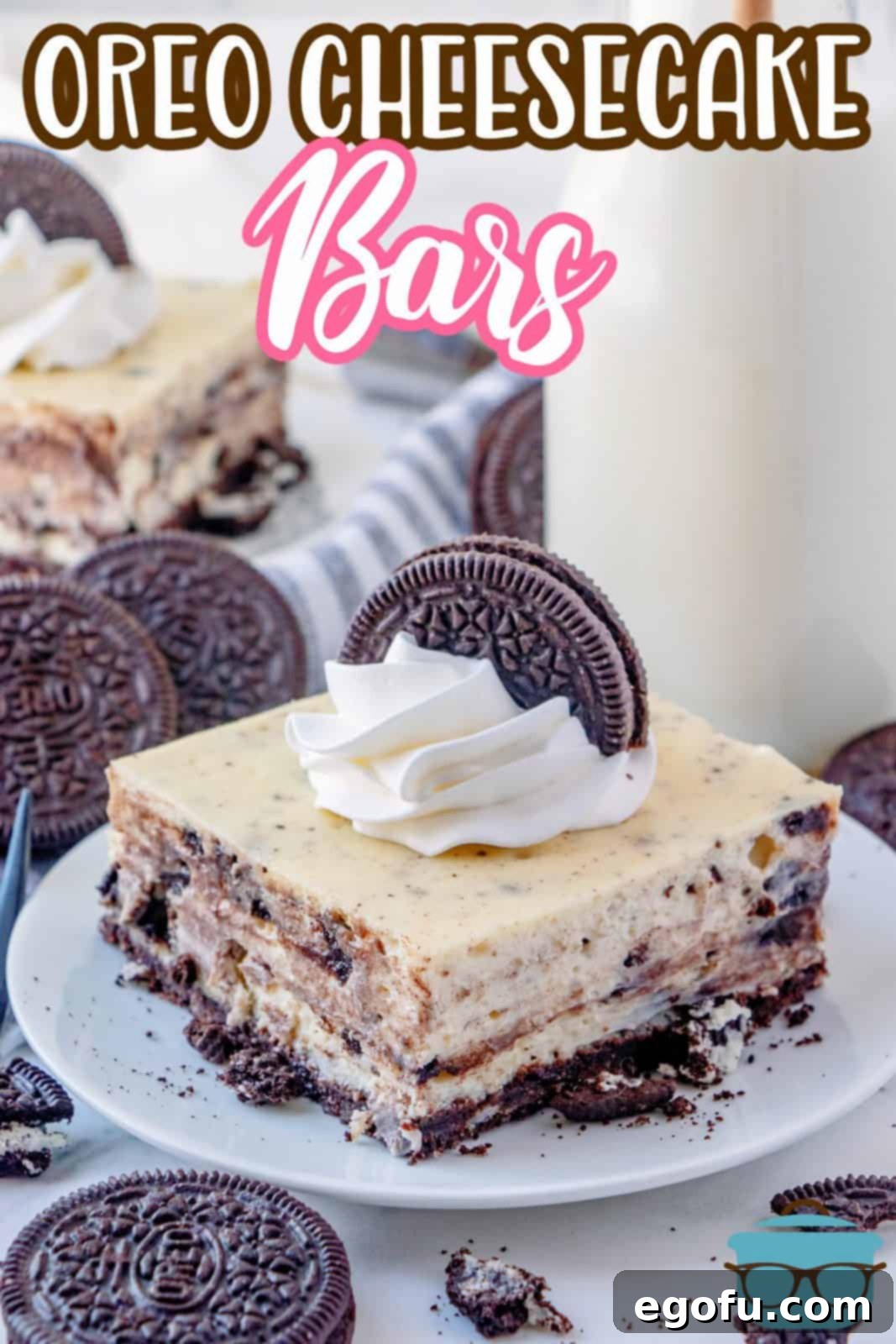 Image of one Oreo Cheesecake Bar on white plate with milk in background topped with whipped topping and oreo cookie.