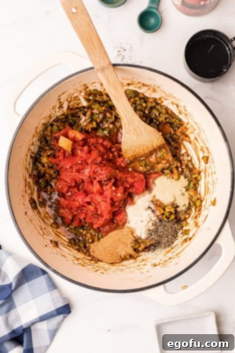 Canned tomatoes, half of the seafood stock, the bay leaves and the seasoning added to vegetables in dutch oven