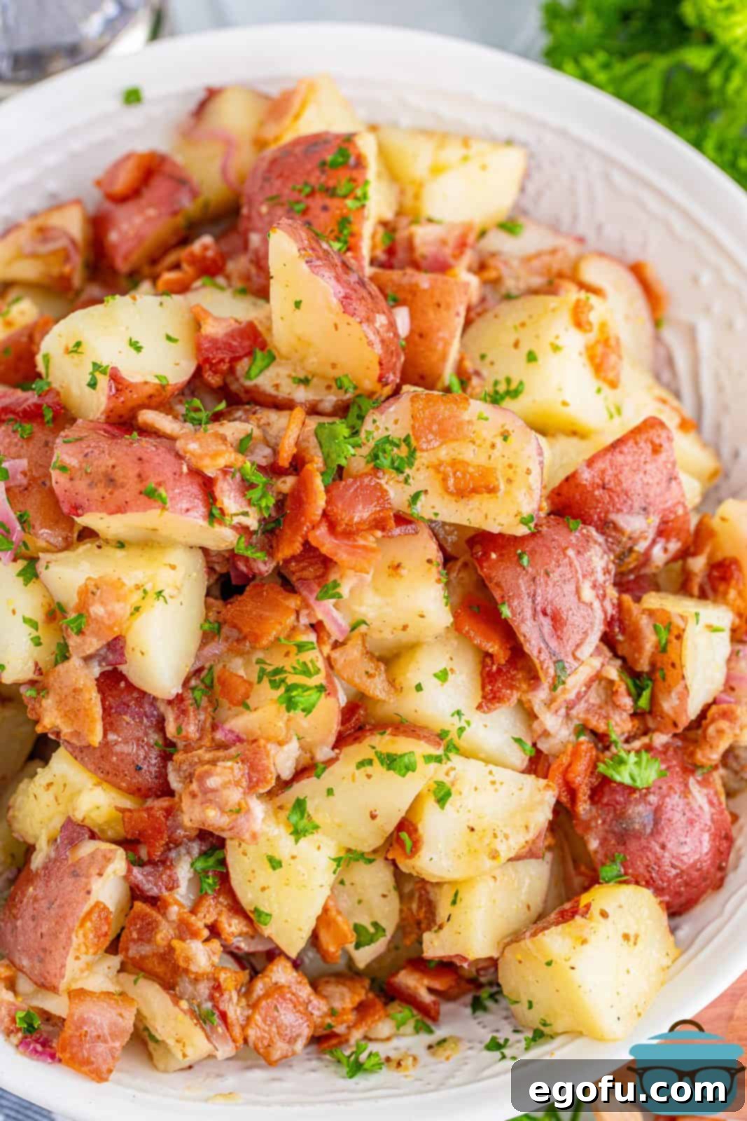 Hearty German Potato Salad 2 Overhead view of homemade German Potato Salad in a white serving bowl, garnished with fresh parsley.