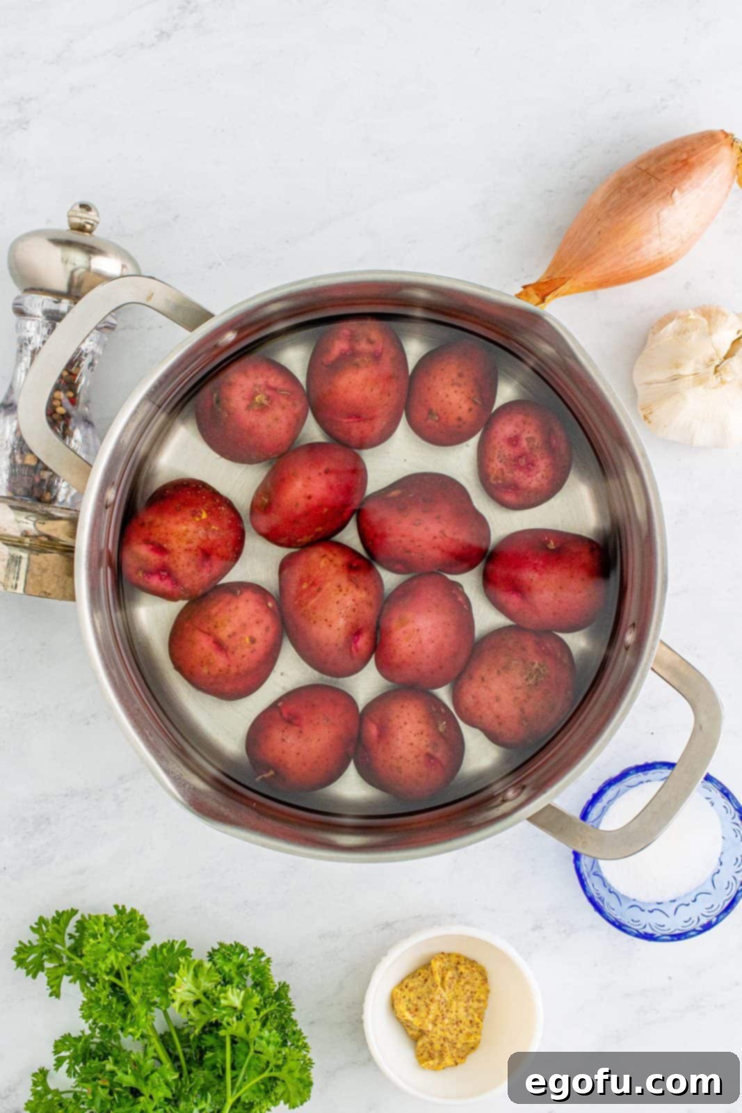 Hearty German Potato Salad 5 Red potatoes submerged in cold water in a large metal cooking pot on a stovetop.