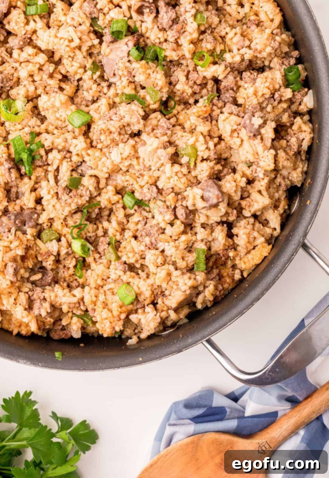 A close-up, inviting shot of half a pan of finished Dirty Rice, with a serving spoon resting enticingly on the side, ready for hungry diners to enjoy.
