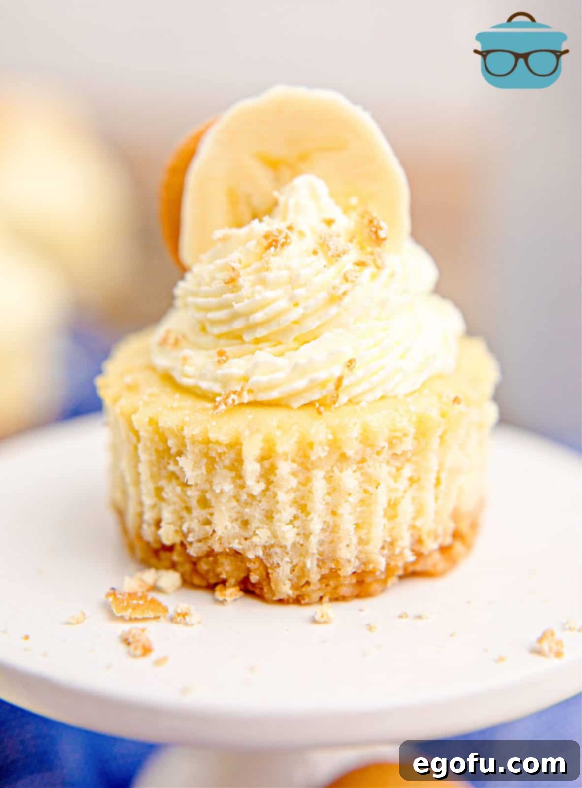 One Mini Banana Pudding Cheesecake on cupcake stand with whipped topping on top and a sliced banana, ready to be enjoyed.