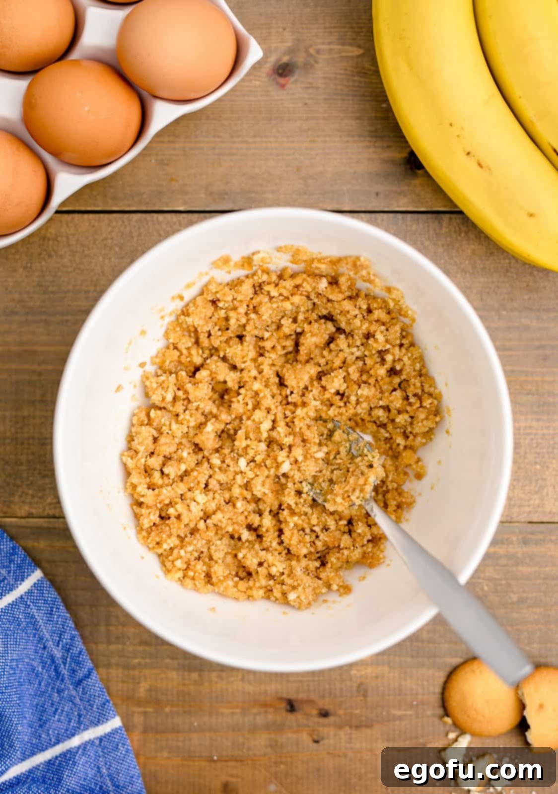 Vanilla wafer crumbs and butter mixed together in a white bowl, showing the consistency for the cheesecake crust.