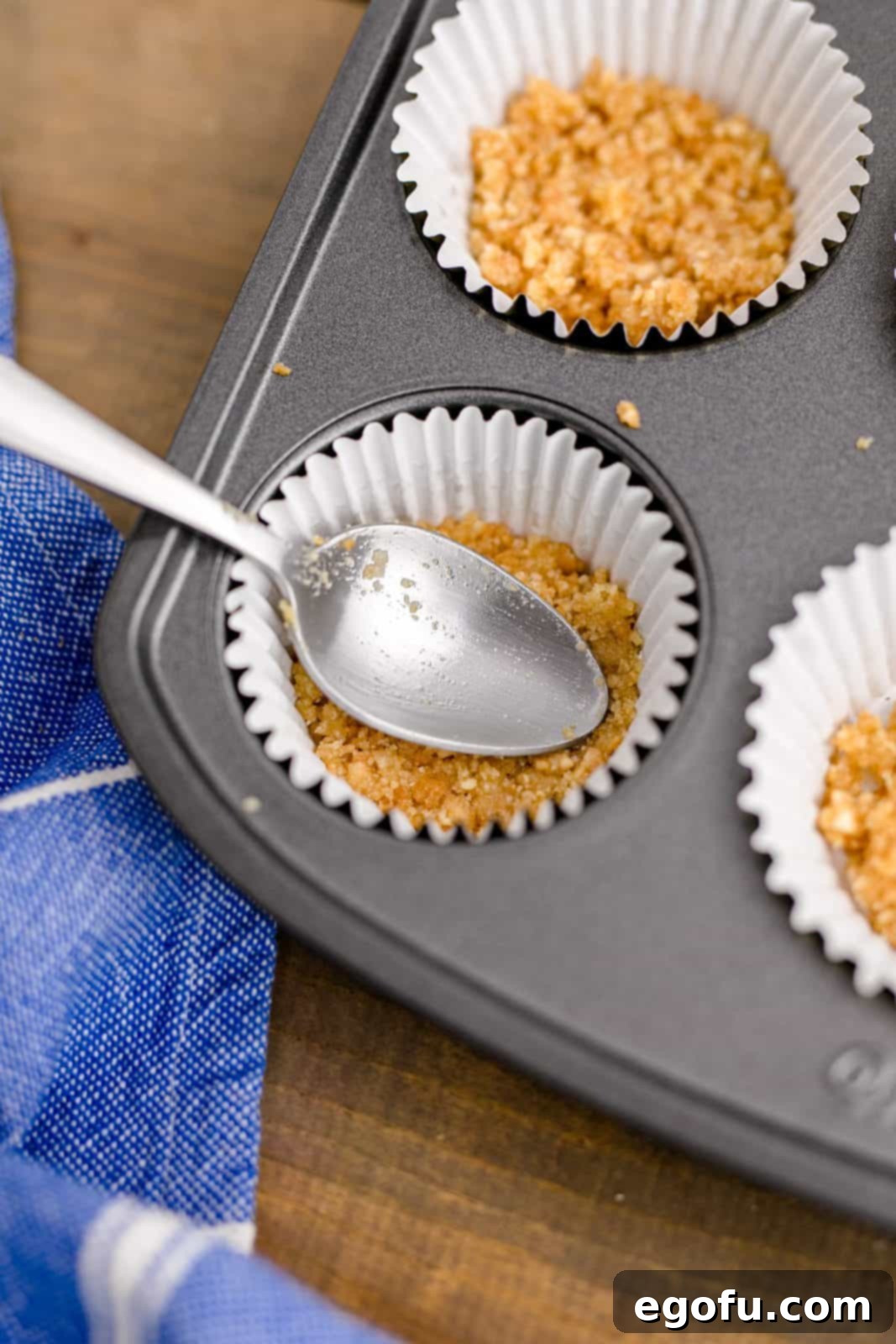 Crumb mixture being pushed down into paper liners in a muffin tin, illustrating the crust-making process.