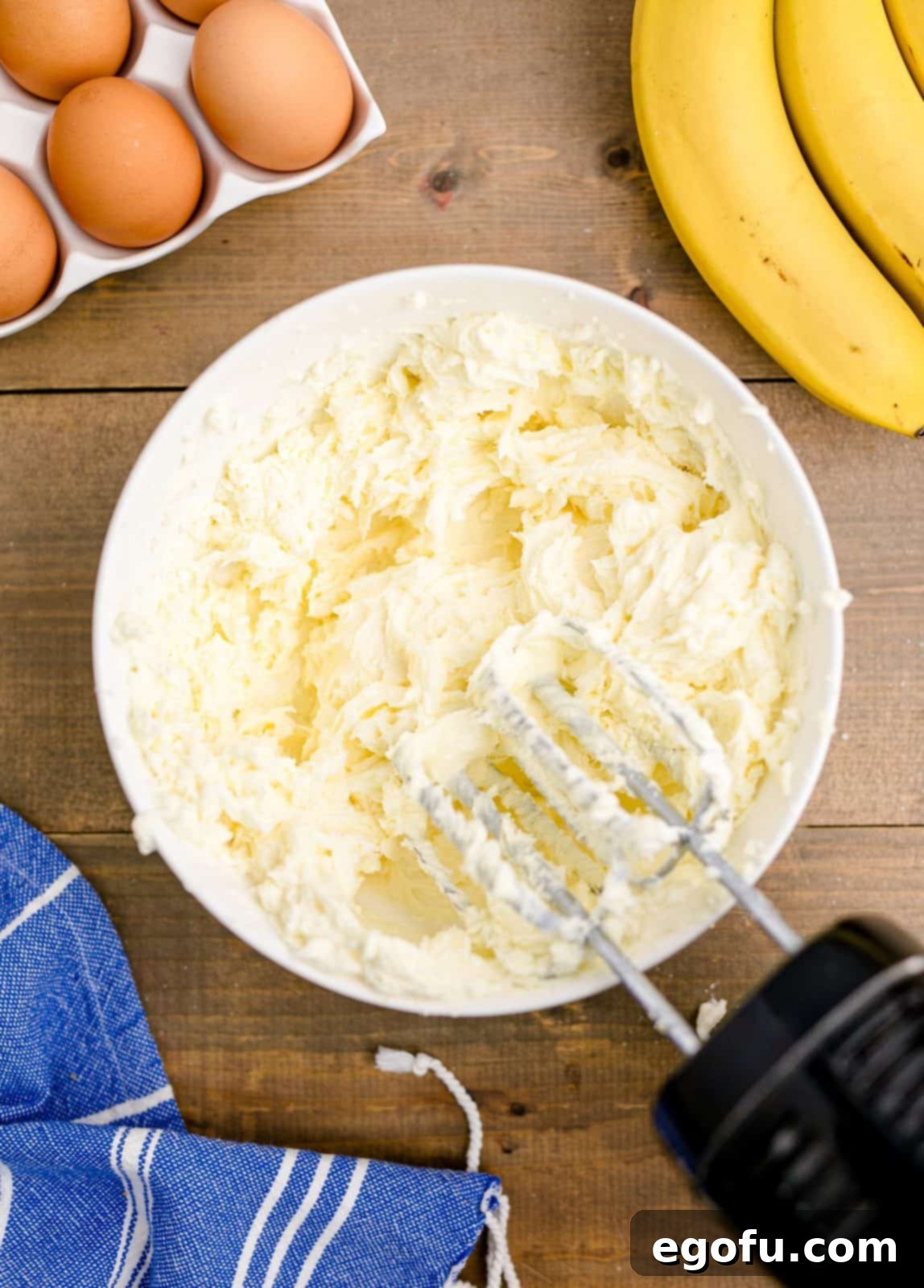 Cream cheese and sugar blended together in a white bowl with a handheld electric mixer, achieving a smooth consistency.