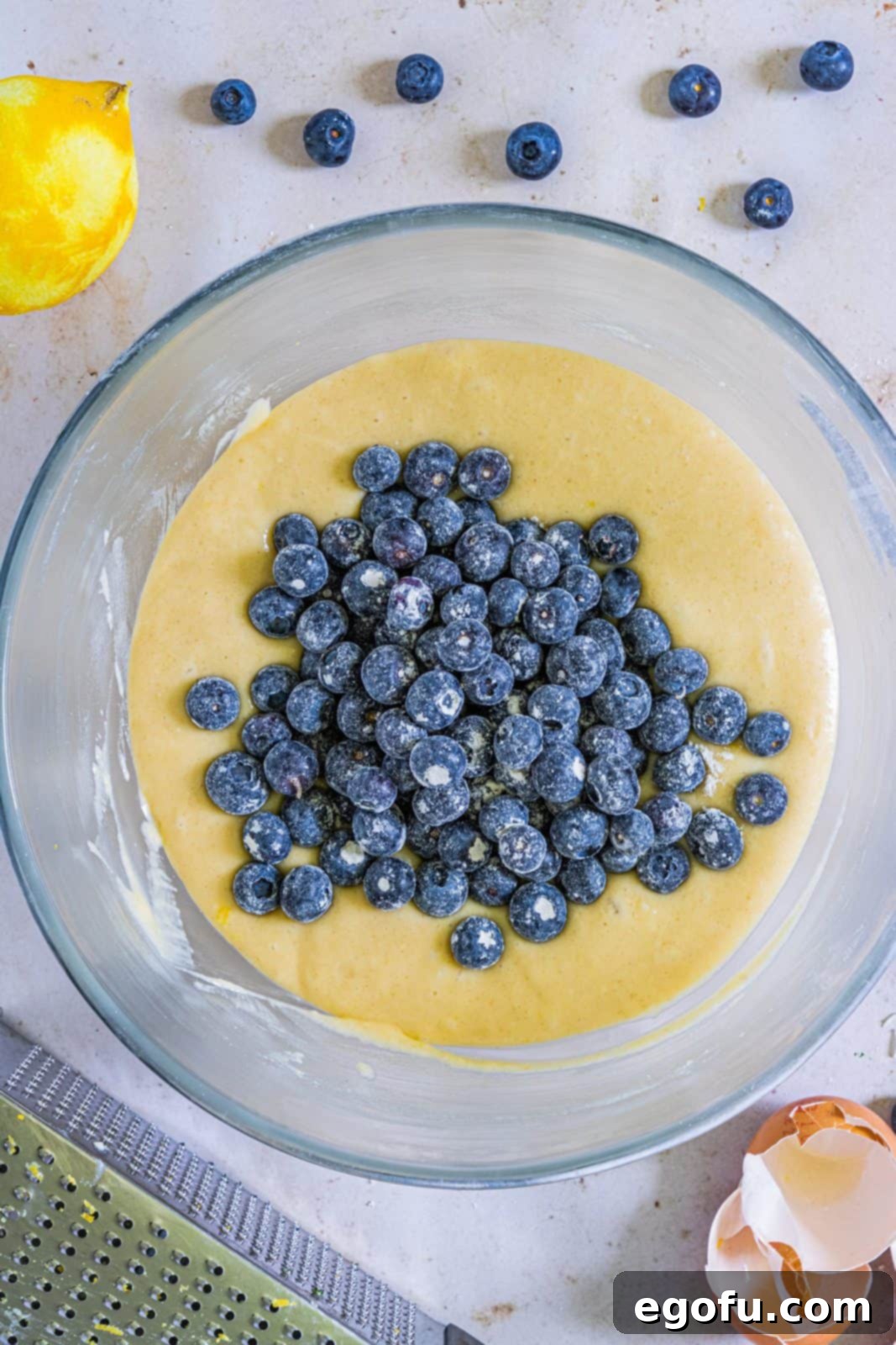 fresh flour coated lueberries added to cake batter in bowl.