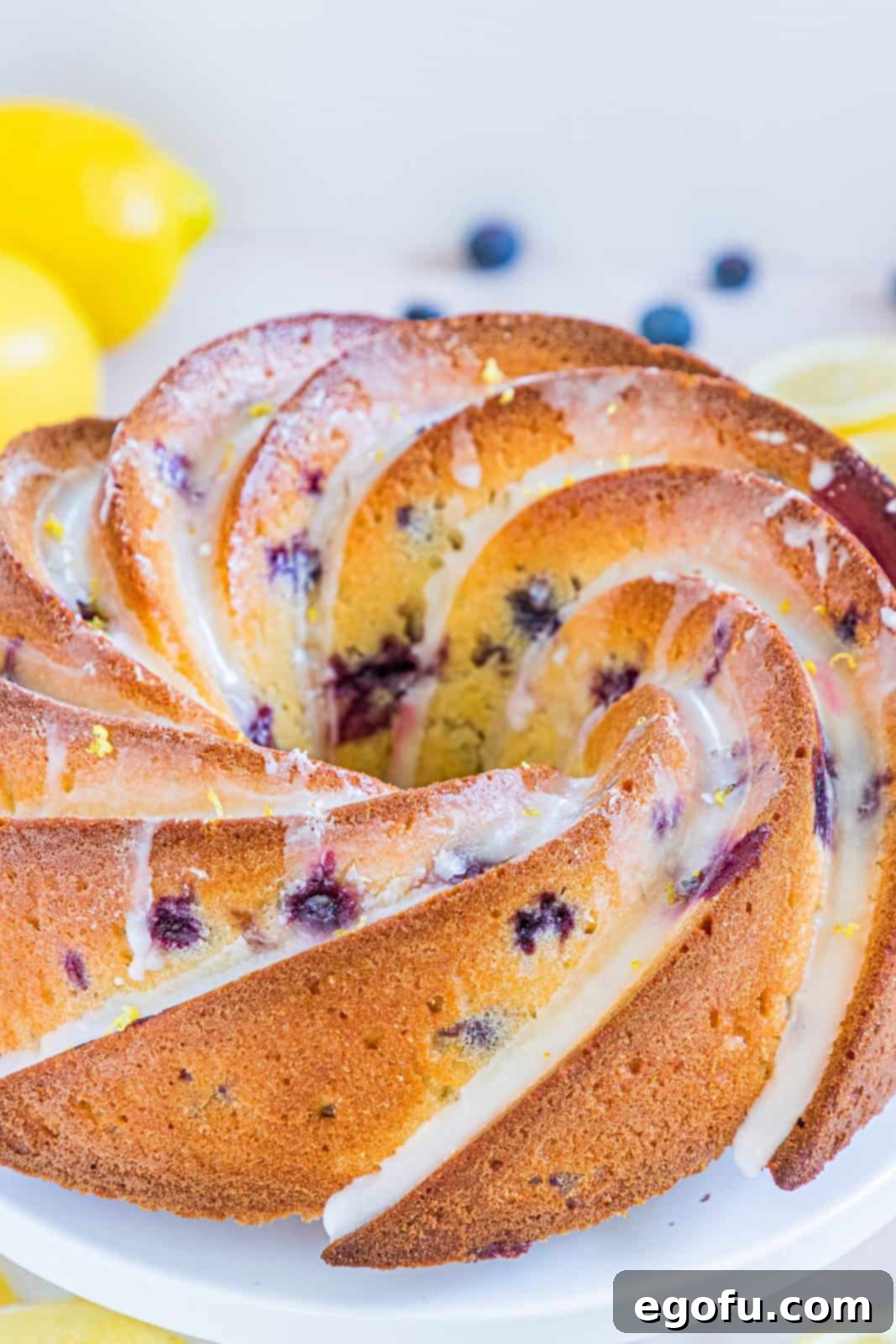Finished Lemon Blueberry Pound Cake with glaze on a white cake stand.