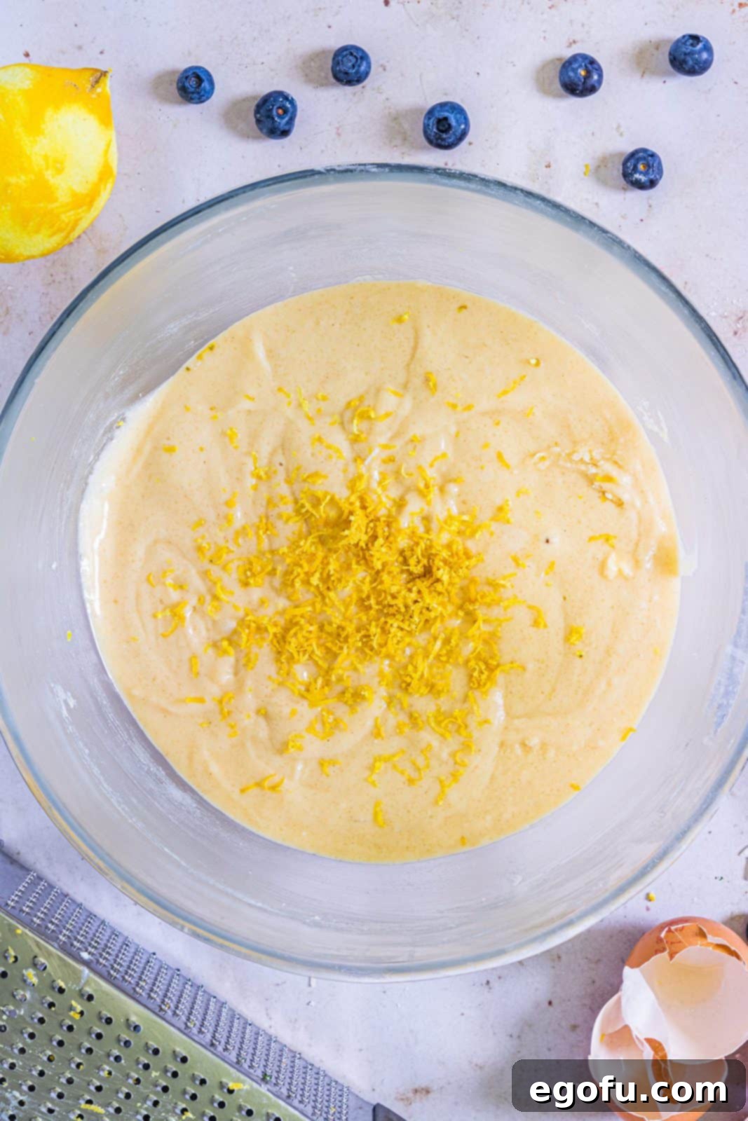 Lemon zest added to cake batter in clear bowl.