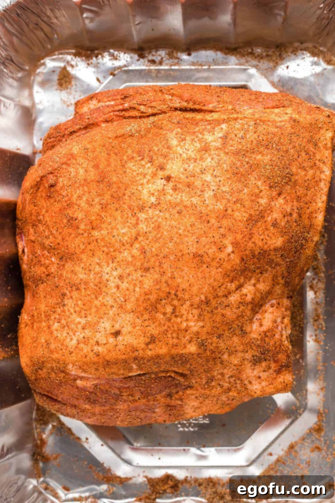 Dry rub rubbed over pork shoulder in metal baking pan.