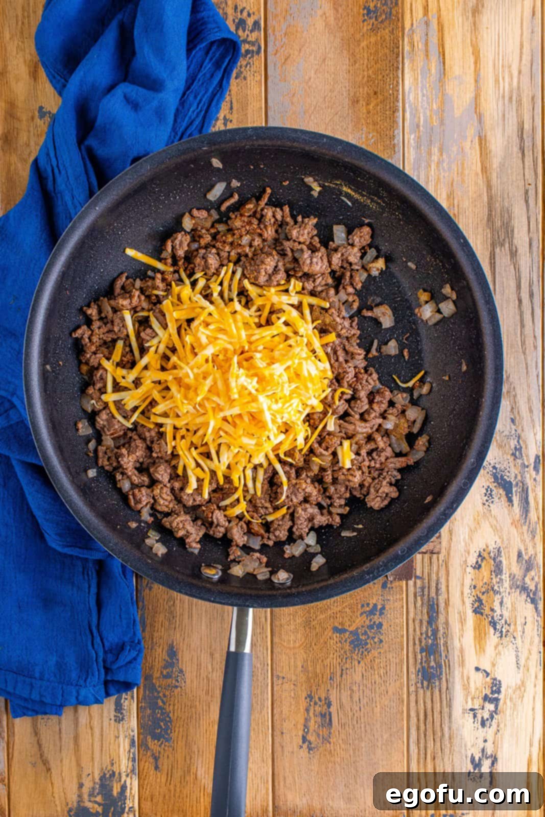 Effortless Taco Bake 8 shredded cheese added to beef mixture in skillet.