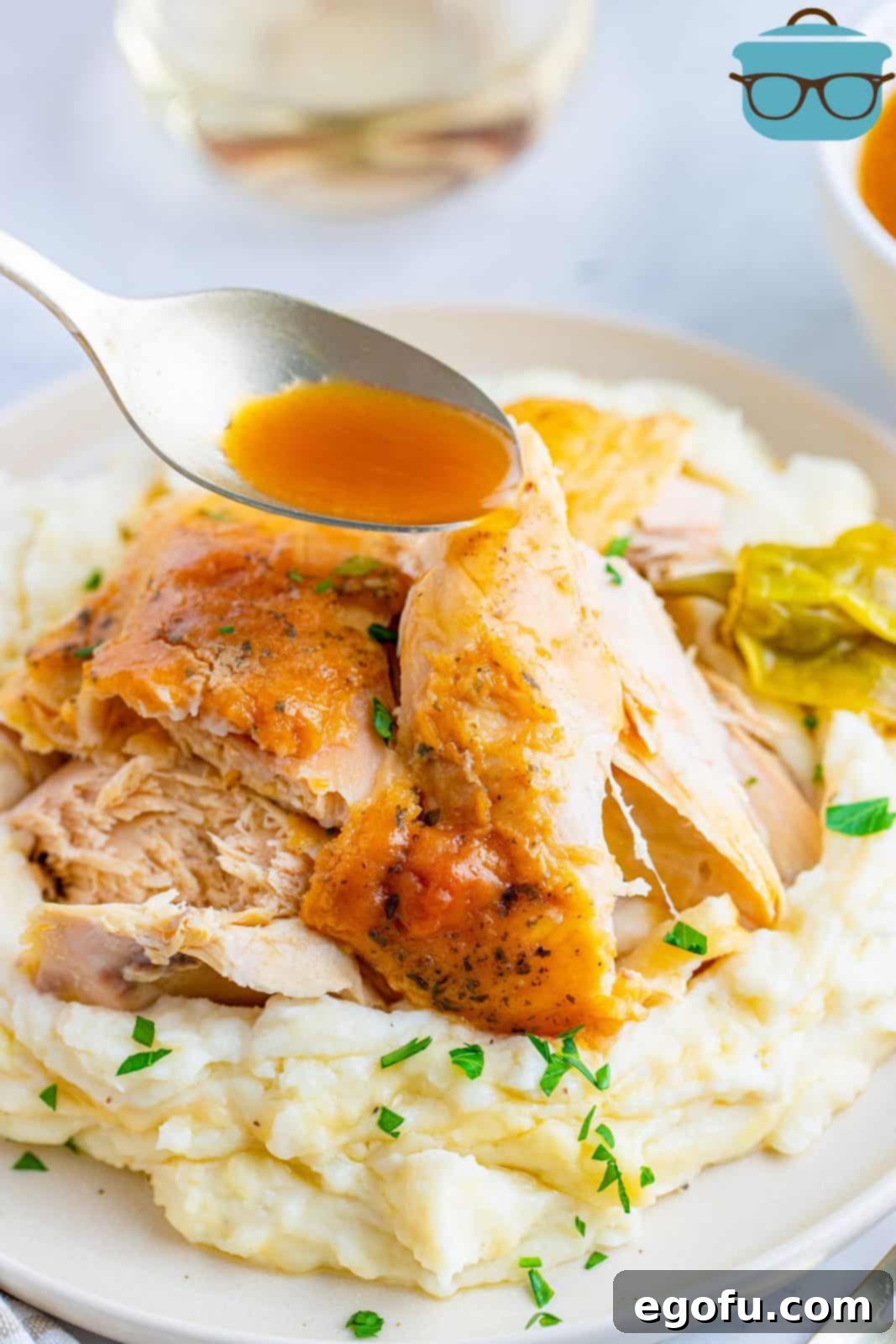 Spoon dripping gravy over chicken on plate with potatoes