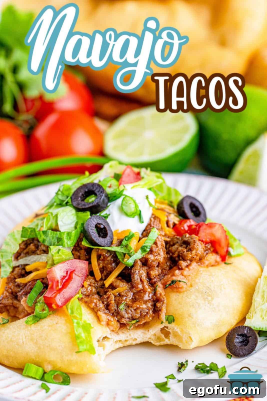 A beautifully presented Navajo Taco on a white plate, garnished with a sliced lime and fresh whole tomatoes in the background, highlighting its vibrant toppings.