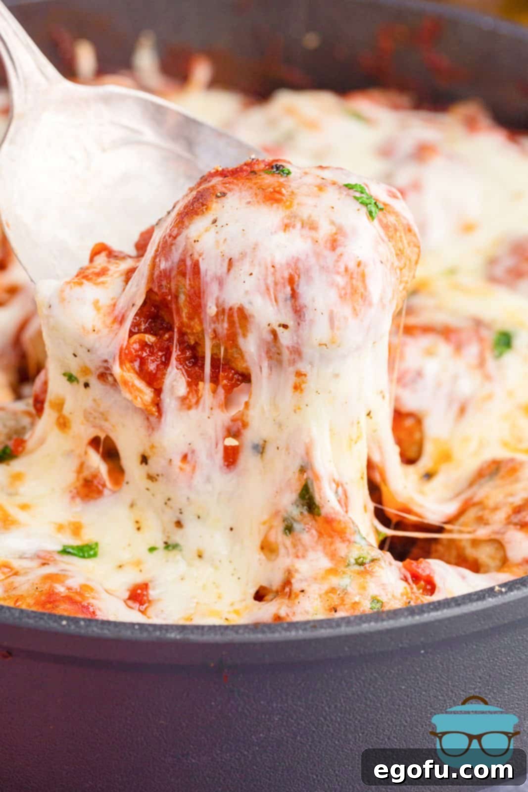 Easy Cheesy Skillet Meatballs 8 Spoon lifting up a meatball from the Meatball Parmesan Skillet, showcasing the delicious melted cheese pull.