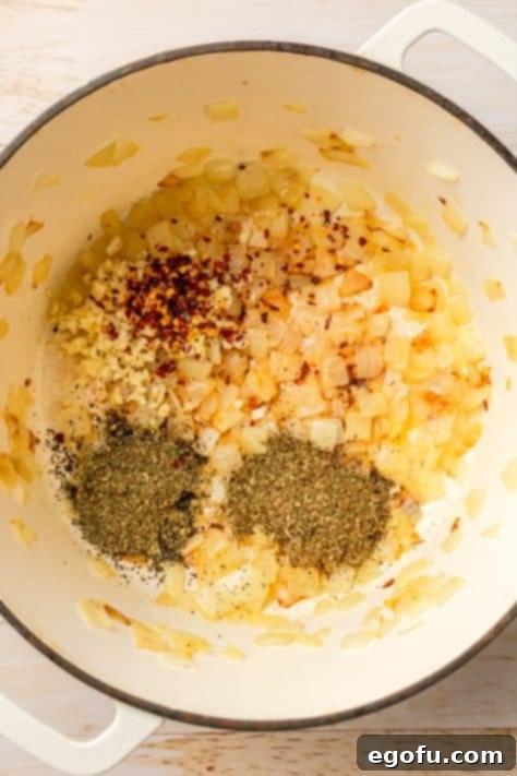 A pot with sautéed onions, minced garlic, dried basil, dried oregano, and red pepper flakes.
